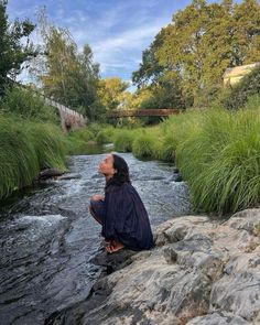 a man sitting on top of a rock next to a river filled with lots of water