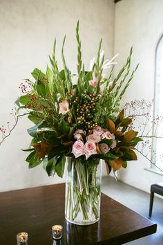 a vase filled with lots of flowers on top of a wooden table next to candles