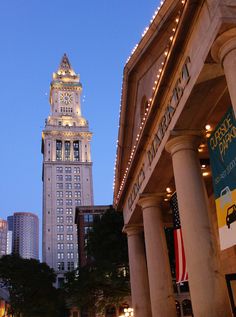 a tall building with a clock tower in the background at dusk, surrounded by other buildings