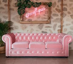 a pink couch sitting in front of a wall with a neon sign on it's side