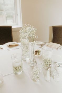 the table is set with wine glasses, candles and baby's breath flowers in vases