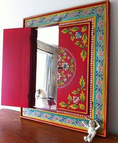 a colorful mirror sitting on top of a wooden table next to a window and stuffed animal