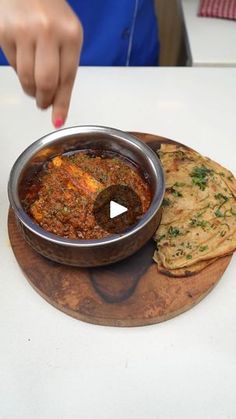 a bowl of food sitting on top of a wooden platter next to a piece of bread