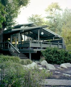 a house that is next to some trees and rocks in front of it with stairs leading up to the upper level