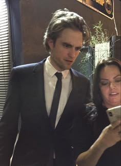 a man in a suit and tie looking at his cell phone while standing next to a woman