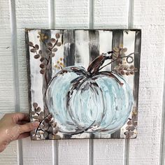 a painting of a blue pumpkin is hanging on a white wall with leaves and branches