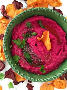 a green bowl filled with beet hummus and chips