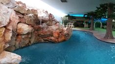 an indoor swimming pool surrounded by rocks and water features a waterfall that runs down the side of it