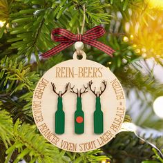 a christmas ornament with three beer bottles hanging from a tree in front of lights