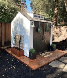 a small shed with potted plants on the front and side, in a backyard