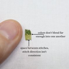 a finger is pointing at the needle on a piece of fabric