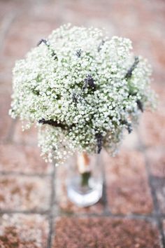 a bouquet of baby's breath in a glass vase on a brick floor,