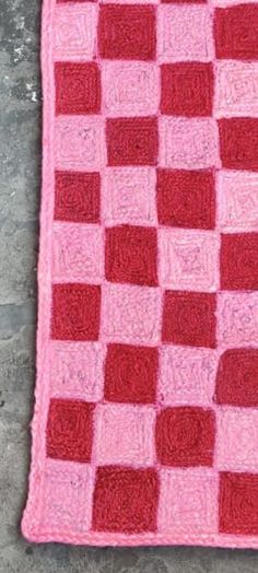 a pink and red crocheted blanket laying on the ground