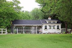 a white house with a black roof and windows in the middle of a grassy field