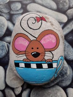 a painted rock with a cartoon mouse in a teacup on top of some rocks