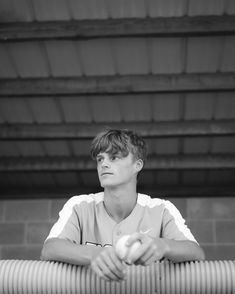 a young man holding an apple while sitting on top of a wooden bench in front of a building