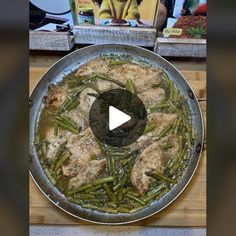 a pan filled with chicken and green beans on top of a wooden table next to a book