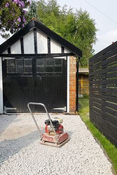 a lawn mower sitting in the gravel next to a building with a black garage behind it