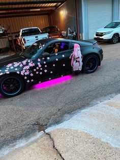 a black car with pink flowers painted on it's side parked in front of a garage