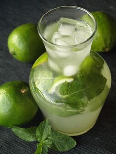 a pitcher filled with ice and limes on top of a table next to some mint leaves