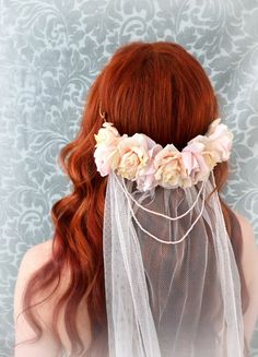 a woman with long red hair wearing a veil and flowers in her hair is seen from the back