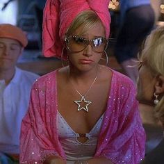 a woman wearing sunglasses and a pink towel on her head with other people in the background