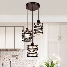 three lights hanging over a kitchen island with white cabinets and marble counter tops in the background