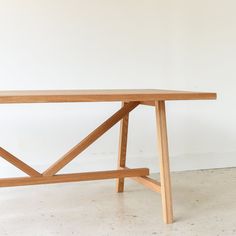 a wooden table sitting on top of a cement floor next to a white wall in an empty room