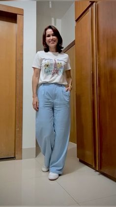 a woman standing in front of wooden closets wearing blue pants and a white t - shirt