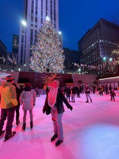 people skating on an ice rink in front of a lit christmas tree and skyscrapers