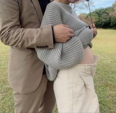 a man and woman standing next to each other in the grass with an umbrella over their heads