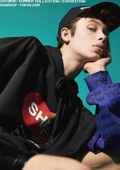 a young man with his hand on his chin wearing a black hat and blue shirt