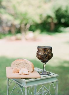 a table with bread and a wine glass on it in the middle of a park