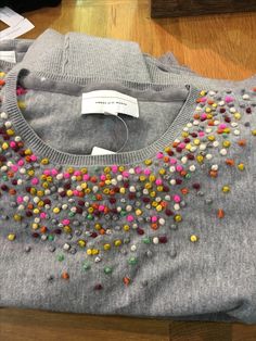 a gray sweater with multicolored beads on it