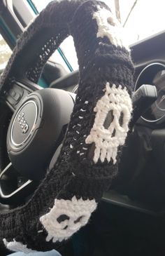 the steering wheel cover is crocheted with white and black yarn, which makes it look like a skull