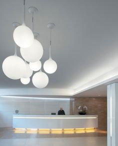 a man standing in front of a white counter with lights hanging from it's ceiling