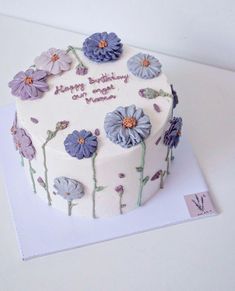 a white cake with purple flowers on it sitting on a table next to a card