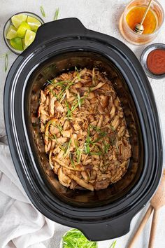 a crock pot filled with meat and garnish next to some sauces