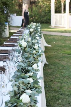 a long table with white flowers and greenery is set up for an outdoor event