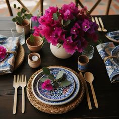 the table is set with blue and white plates, silverware, and pink flowers