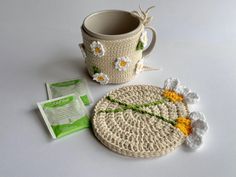 a crocheted coaster and coffee cup holder on a white surface with a tea bag next to it