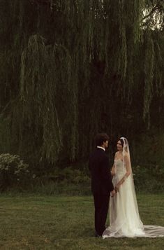 a bride and groom standing in front of a willow tree