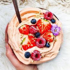 a person holding a dessert with strawberries, raspberries and blueberries on top