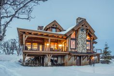 a large log home in the middle of snow covered ground with trees and lights on