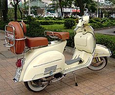 a white scooter parked on the sidewalk in front of some bushes and trees