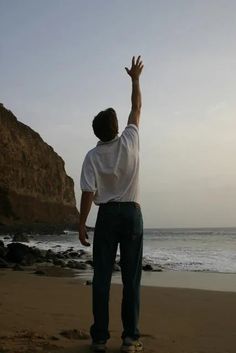 a man standing on top of a beach next to the ocean reaching for a frisbee