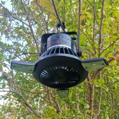 an electric fan hanging from the ceiling in front of trees