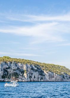 a sailboat floating in the ocean next to a rocky island