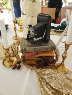 an old camera is sitting on top of books and candles at a table with gold sequins