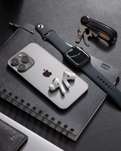 an iphone with earbuds attached to it sitting on top of a book next to a watch